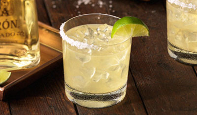 Margarita on the rocks with salt and a lime and part of a tequila bottle in the background.