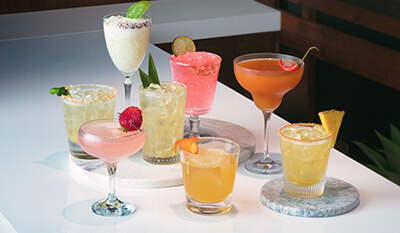Eight different cocktails sitting on a white table.