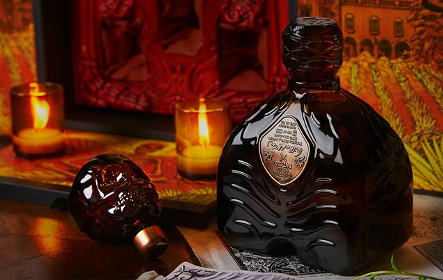 Close up of the Patrón X Guillermo del Toro tequila bottle with two small candle lit behind it.