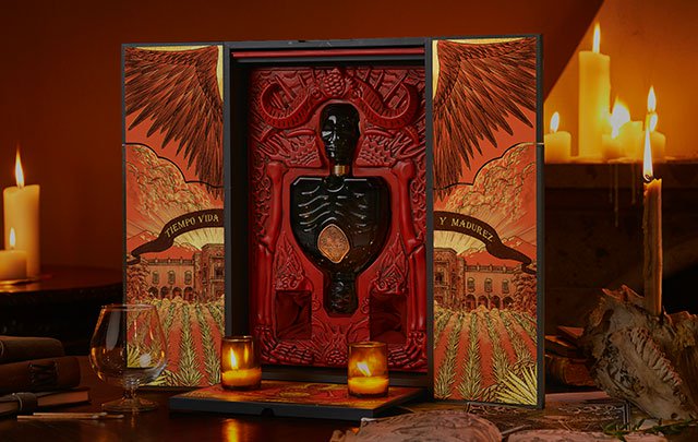 Opened box of Patrón X Guillermo del Toro tequila in a room with lit candles.