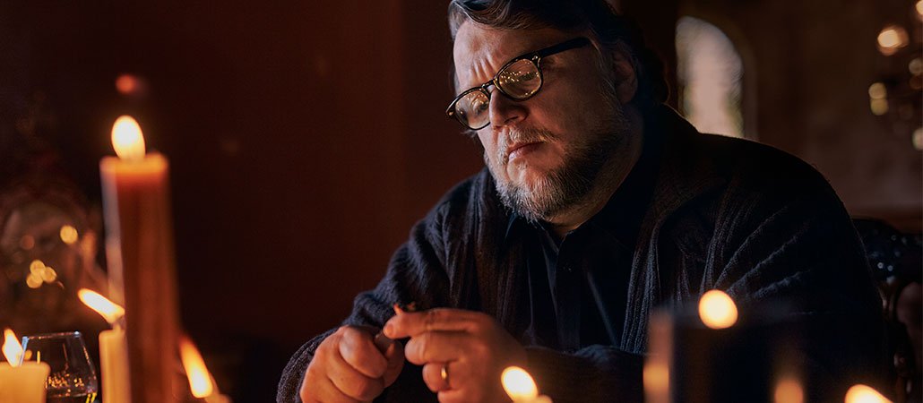 Man with glasses sitting at a table surrounded by lit candles.